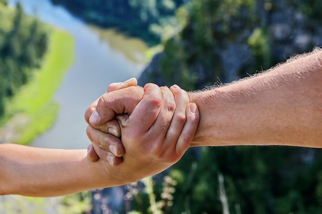 La mano maschio abbraccia la mano femminile sullo sfondo del paesaggio naturale.