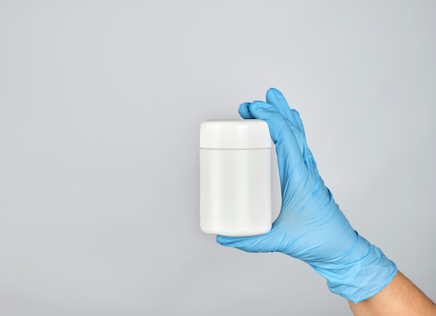 La mano nel guanto sterile blu tiene il barattolo di plastica bianco con le pillole