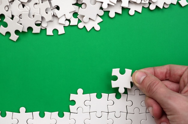 La mano piega un puzzle bianco e una pila di pezzi di puzzle non letti si trova sullo sfondo della superficie verde