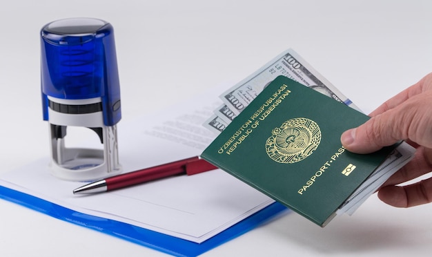 La mano porge il passaporto dell'Uzbekistan con dollari USA sullo sfondo dei documenti