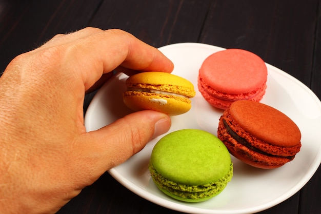 La mano prende i biscotti del macaron sulla superficie nera