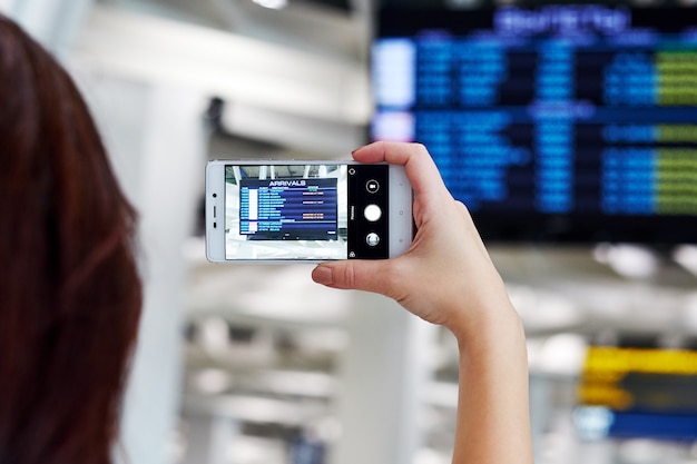 La mano prende la foto sullo smartphone in aeroporto. Sullo schermo, l'orario di partenza del volo