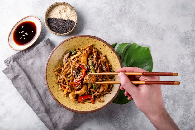 La mano prende le bacchette asiatiche di soba di grano saraceno con verdure, funghi e pollo