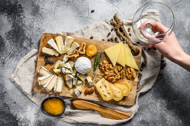 La mano prende un pezzo di formaggio da un piatto di formaggi servito con noci e fichi. Sfondo grigio. Vista dall'alto