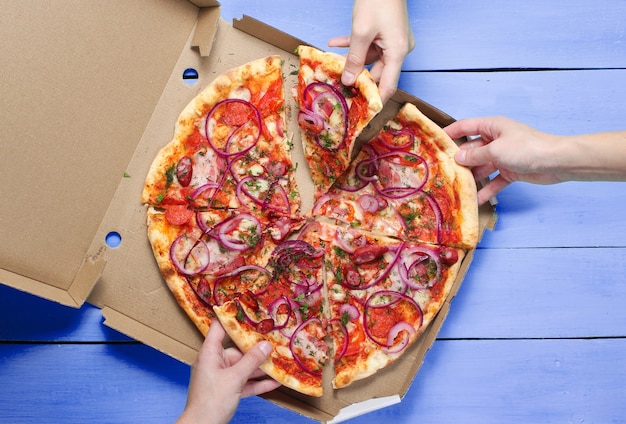 La mano prende un pezzo di pizza su un tavolo blu