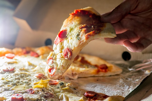 La mano prende una fetta di pizza fresca tirando il formaggio fuso fuori dalla scatola Consegna del cibo