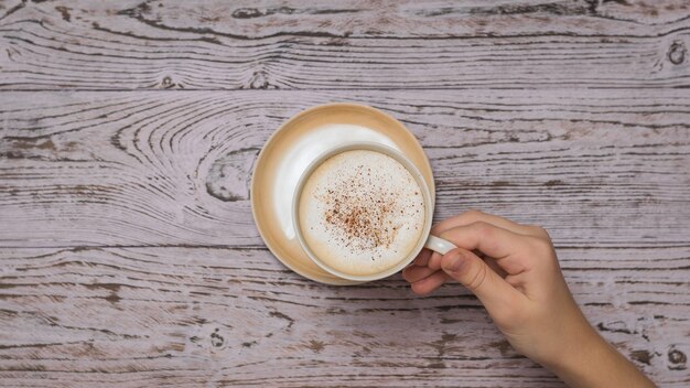 La mano prende una tazza di caffè dal tavolo di legno