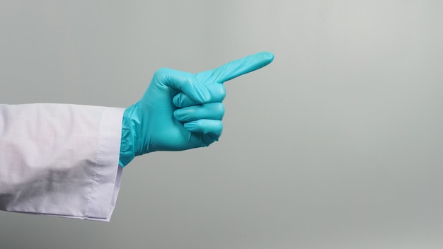 La mano punta il dito e indossa un camice da medico e un guanto medico blu su sfondo grigio. Riprese in studio.