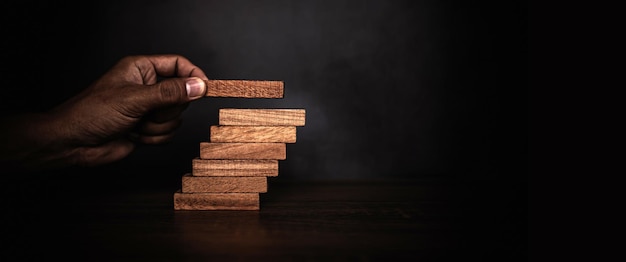 La mano ravvicinata sta posizionando una torre di blocchi di legno impilata sul gradino delle scale