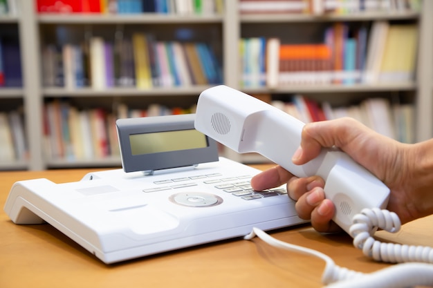 La mano solleva il telefono e preme il pulsante sul telefono dell'ufficio.