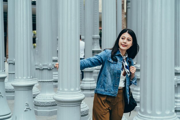 la mano sorridente della ragazza sul lampione bianco è vagare tra le opere d'arte rinomate. giovane donna felice circondata da sculture che cammina e si guarda intorno all'arte dell'installazione a la.