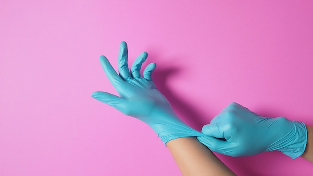La mano sta tirando guanti chirurgici o guanti in lattice blu su sfondo rosa.