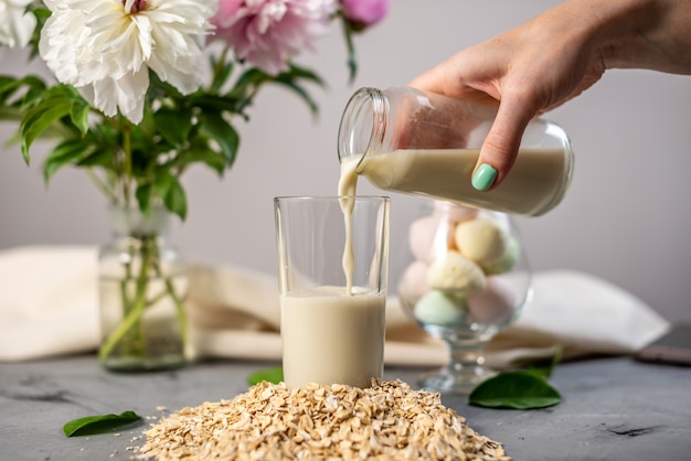 La mano sta versando in un bicchiere di latte di farina d'avena vegetale naturale