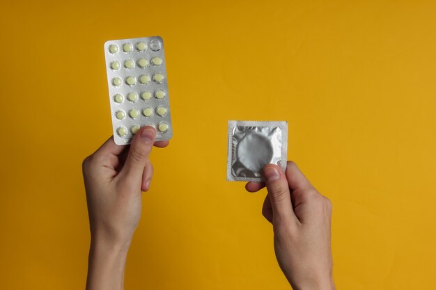 La mano tiene i preservativi nella confezione, pillole anticoncezionali su carta gialla