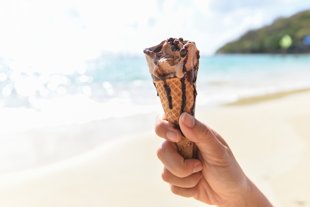 La mano tiene il gelato sul fondo della spiaggia