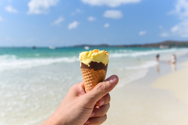 La mano tiene il gelato sul fondo della spiaggia