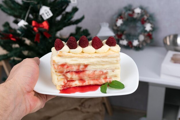 La mano tiene il piattino con un pezzo di torta di frutta sullo sfondo dell'albero di Natale. Torta con frutti di bosco.