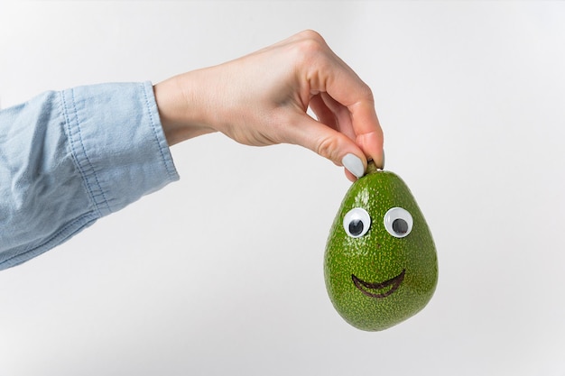 La mano tiene il sorriso di avocado su sfondo bianco Avocado con faccia buffa