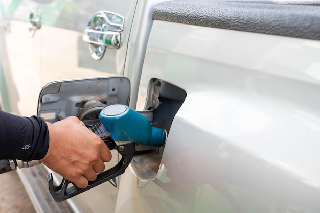 La mano tiene l'ugello per rifornire di carburante l'auto nella stazione di servizio