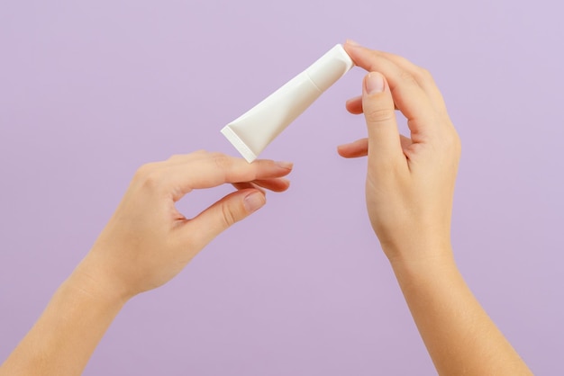 La mano tiene la battaglia di crema di plastica isolata su sfondo lilla Concetto di bellezza Tubo di imballaggio per prodotti cosmetici