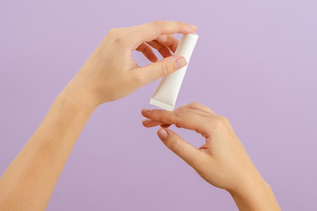 La mano tiene la battaglia di crema di plastica isolata su sfondo lilla Concetto di bellezza Tubo di imballaggio per prodotti cosmetici