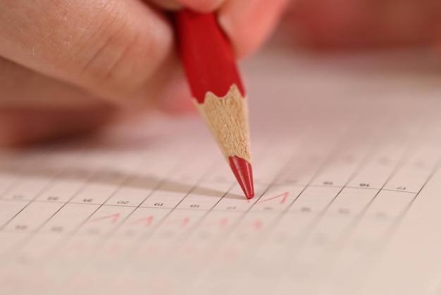 La mano tiene la matita rossa e scrive sul calendario o sulla carta di prova