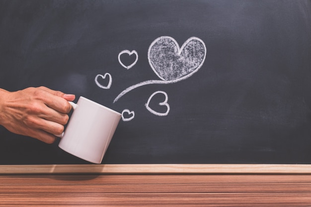 La mano tiene la tazza di caffè e la forma del cuore è sulla lavagna