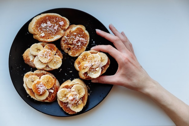 La mano tiene la torta di banana alla frutta fatta in casa per la colazione sul piatto di ceramica nera Vista dall'alto del fuoco selettivo