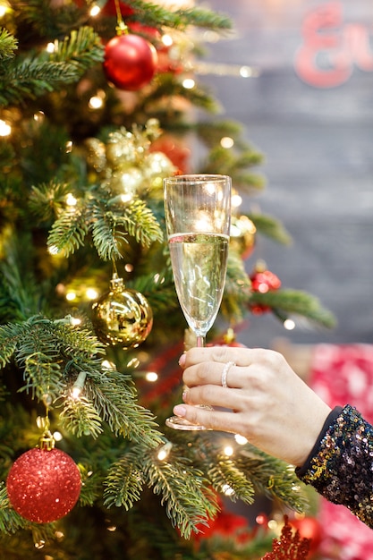 La mano tiene un bicchiere di champagne sullo sfondo di un albero di Natale decorato