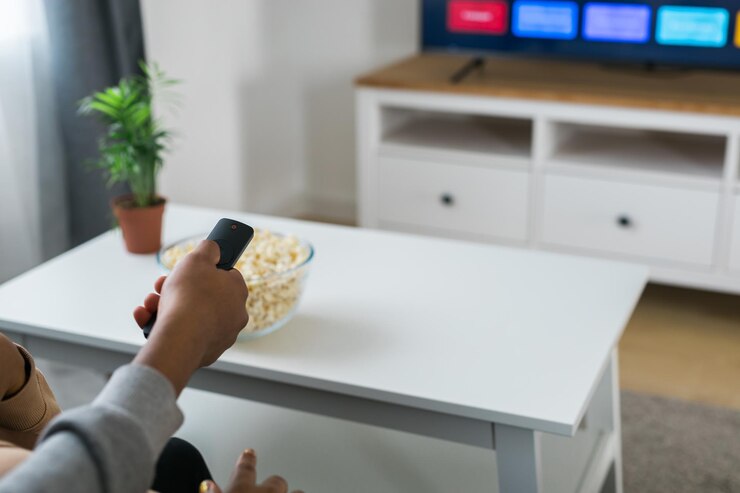 La mano tiene un telecomando mentre una ciotola di popcorn si trova su un tavolo bianco in un salotto moderno