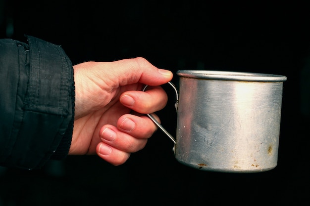 La mano tiene un vaso metallico su uno sfondo scuro