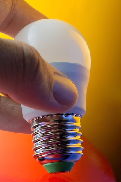 La mano tiene una lampada a LED con base e14 illuminata in diversi colori.