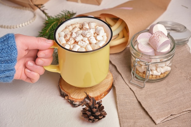 La mano tiene una tazza gialla con cocao e marshmallow