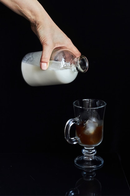 La mano versa il latte dalla bottiglia nel bicchiere con caffè freddo