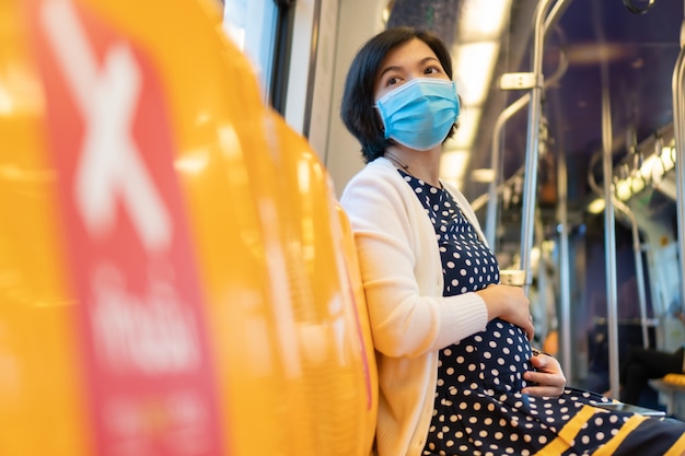 La maschera di protezione asiatica di usura della donna incinta si siede in treno di alianti nella nuova vita normale