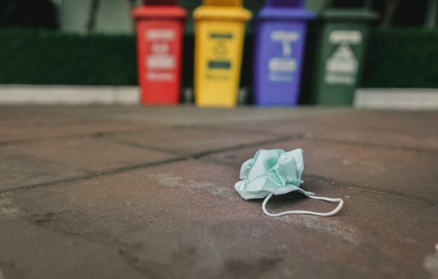 La maschera di protezione medica usata scarta sul pavimento della pavimentazione sul cestino o sui rifiuti vago.