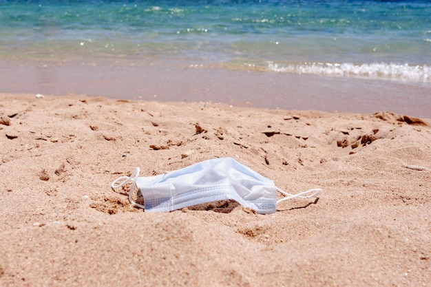 La maschera medica si trova sulla sabbia sulla spiaggia sullo sfondo del mare rimozione della maschera medica usata Giornata in spiaggia durante la pandemia di coronavirus covid19