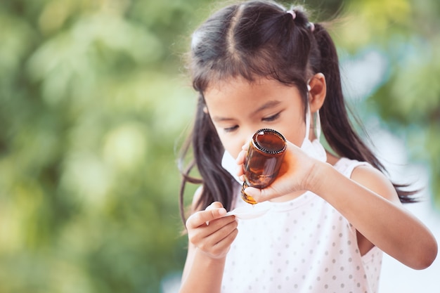 La mascherina protettiva di usura asiatica minuta della ragazza del bambino stava prendendo la medicina dello sciroppo