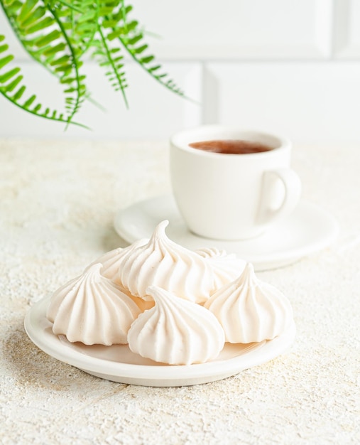 La meringa si trova su un piatto bianco. In sottofondo, una tazza di caffè. Sfondo chiaro.