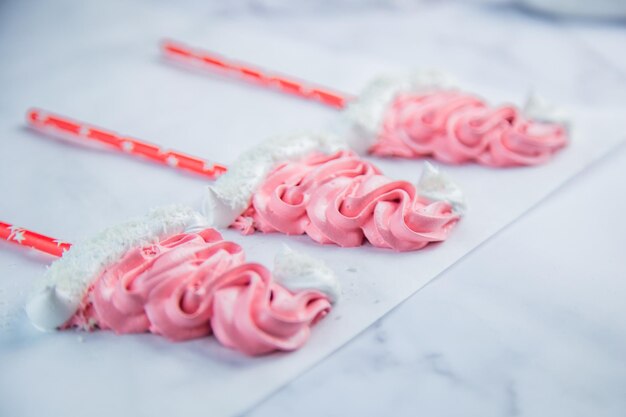 La meringa sotto forma di cappelli natalizi rosa con bumbone bianco e bordo giace su pergamena bianca