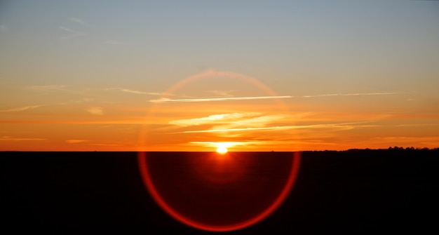 La metà del sole durante l'alba sullo sfondo del cielo caldo Cielo arancione sul campo