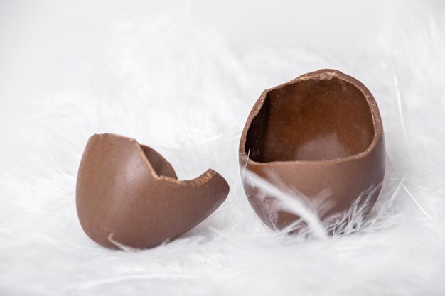 La metà di un uovo di cioccolato vuoto incrinato e un guscio d'uovo vuoto in un nido di piume bianche Dolce tradizione pasquale Vacanze primaverili Pasqua per bambini