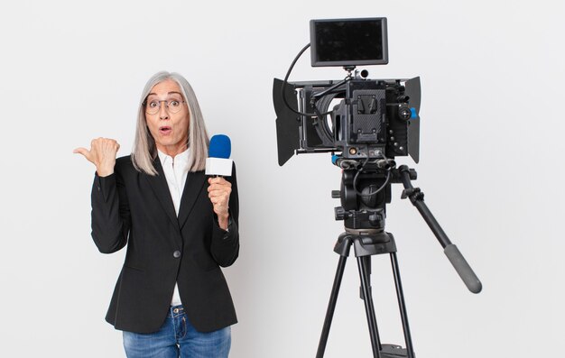 La mezza età capelli bianchi donna guardando stupito incredulo e tenendo un microfono. concetto di presentatore televisivo