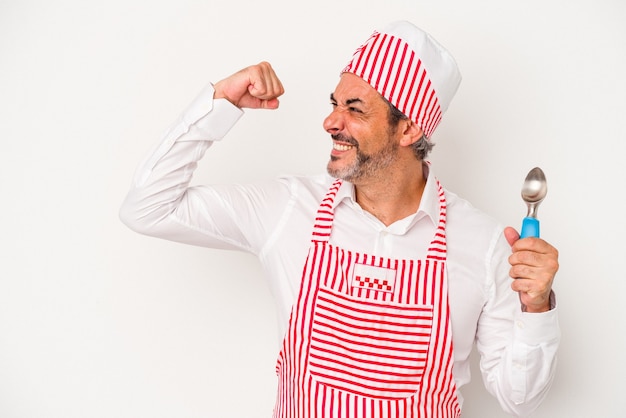 La mezza età caucasica fabbricatore di ghiaccio uomo caucasico tenendo un cucchiaio isolato su sfondo bianco alzando il pugno dopo una vittoria, concetto vincitore.