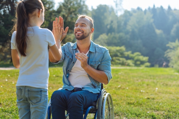 La migliore squadra. Adorabile bambina che dà il cinque al suo affascinante padre con difficoltà motorie mentre trascorre il fine settimana nel parco