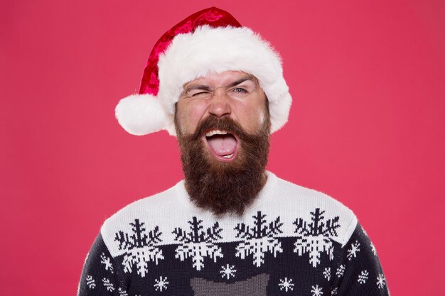 La migliore vacanza. cappello da Babbo Natale uomo barbuto ammiccante. sfondo rosso maglione preferito brutale hipster. divertimento per le vacanze invernali. baffi faccia felice. ritratto di santa uomo con la barba. festa di fine anno. periodo natalizio.