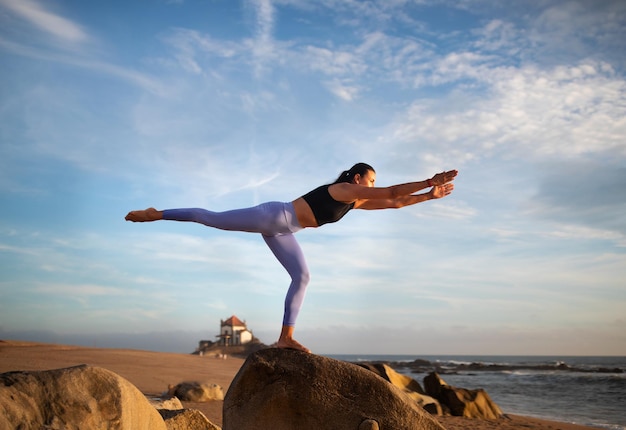 La millenaria signora caucasica sottile in abbigliamento sportivo pratica yoga gode di esercizi di respirazione in equilibrio sul mare