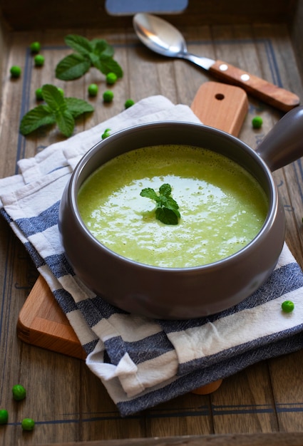 La minestra di crema di dieta casalinga fresca dei piselli e dei broccoli è servito con la menta su un vassoio di legno scuro. Avvicinamento