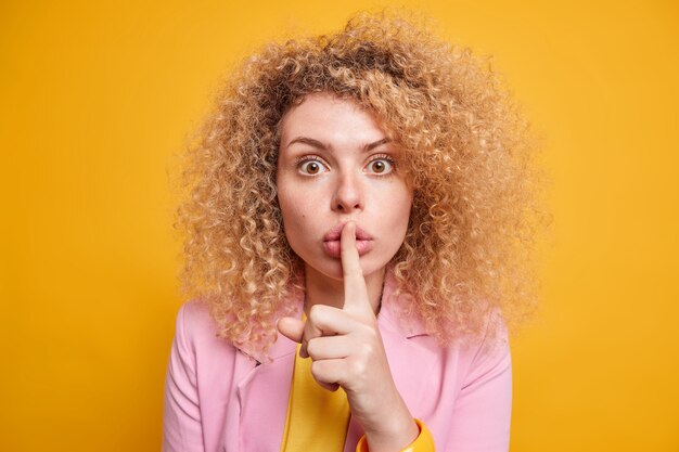 La misteriosa donna europea dai capelli ricci sorpresa dice di stare zitta fa un gesto tabù premendo il dito indice sulle labbra