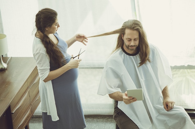 La moglie incinta si taglia i capelli per il marito mentre resta a casa come un bel tono di colore vintage caldo e amorevole in famiglia.